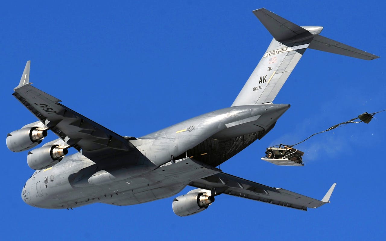 United States Air Force aircraft performing an airdrop maneuver in clear sky.